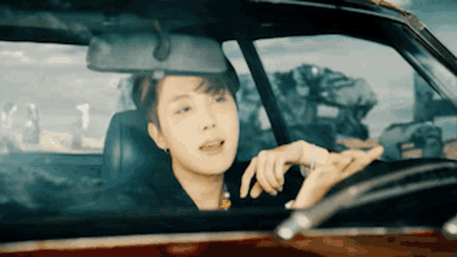 a young man is driving a car with his hand on the steering wheel