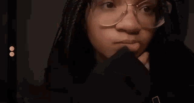 a woman wearing glasses and a black sweater is covering her mouth with her hand .