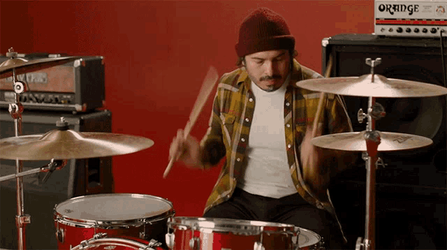 a man playing drums with an orange amplifier in the background
