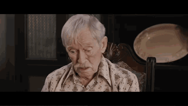 an elderly man with white hair and a mustache is sitting in a chair