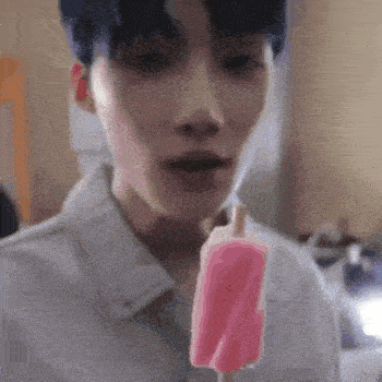a young man with blue hair is eating a pink popsicle