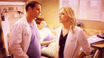 a man and a woman are standing next to each other in a hospital room . the woman is pregnant .