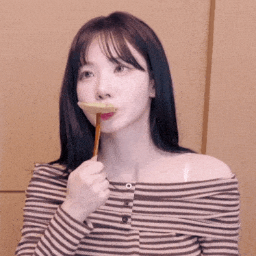 a woman in a striped off the shoulder top is holding a stick in her mouth