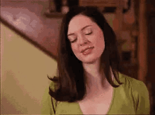 a woman in a green shirt is smiling with her eyes closed and her mouth open .