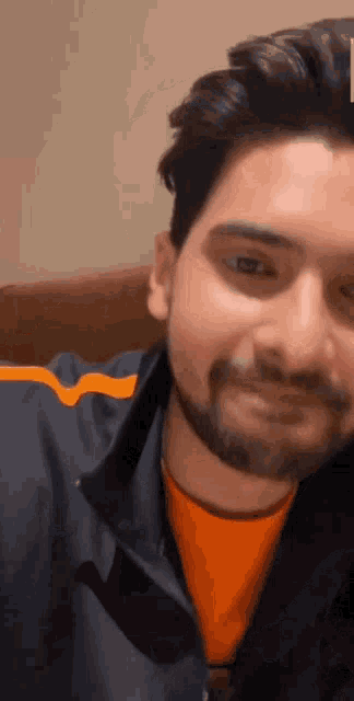 a man with a beard is wearing an orange shirt and a blue jacket .