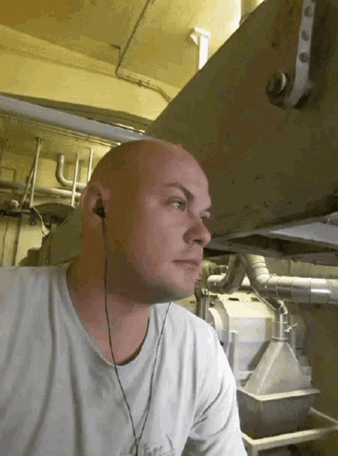 a bald man wearing earbuds looks down at something