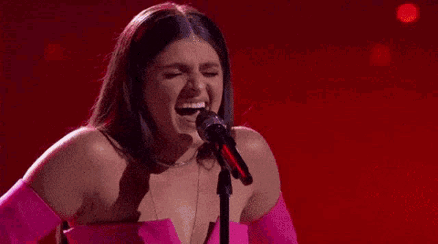a woman in a pink dress singing into a microphone with the name bella denapoli on the bottom right