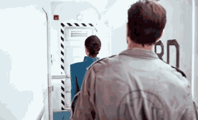 a man and a woman are walking down a hallway next to a door .