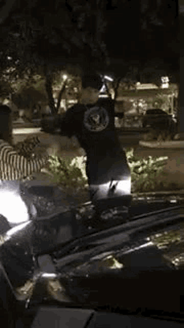 a man in a black shirt is standing next to a car at night .
