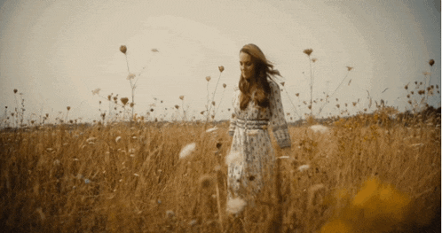 a woman in a white dress is walking through a field of tall grass and flowers