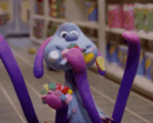 a stuffed animal with purple tentacles is holding candy in its mouth .