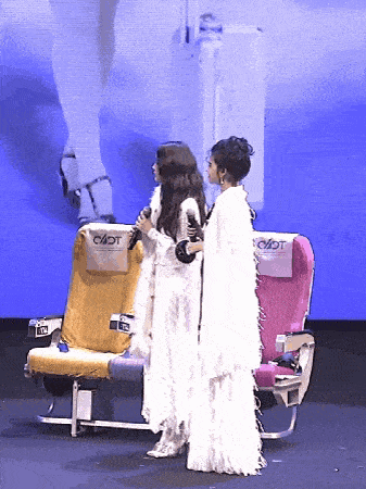 two women standing next to airplane seats that say cadt on them