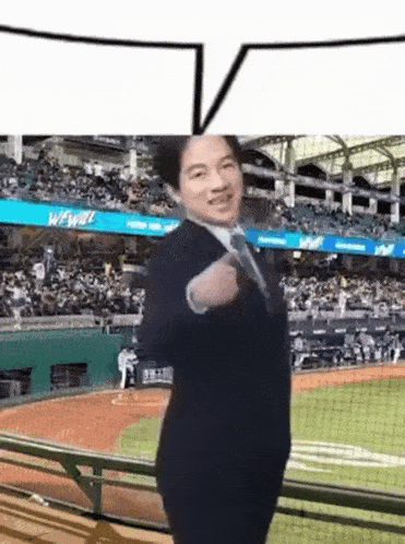 a man in a suit and tie is standing on a baseball field with a speech bubble above him .