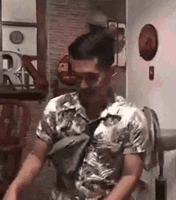 a man in a hawaiian shirt is standing in a room with a bag on his shoulder .