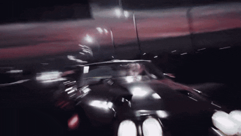 a black car is driving down a dark street at night