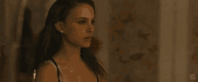a woman in a black tank top is standing next to a bed in a room .