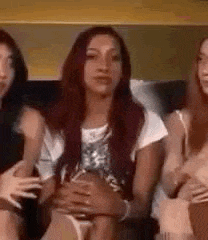 three women are sitting on a couch holding each other 's stomachs .