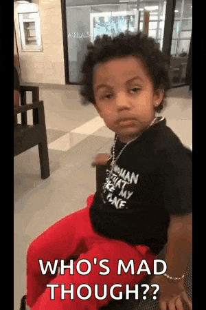 a little boy is sitting on a bench and making a funny face while wearing a black shirt and red pants .