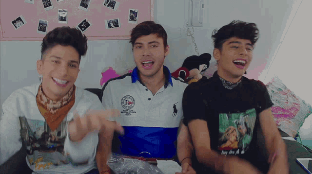 three young men are sitting on a bed and one of them is wearing a polo shirt with the word polo on it