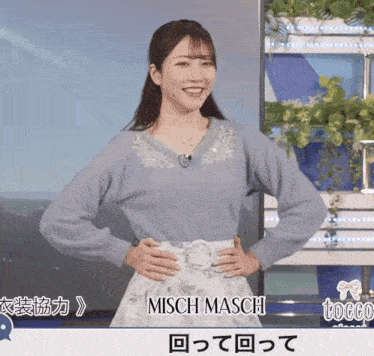a woman wearing a blue sweater and a white skirt stands in front of a sign that says misch mach