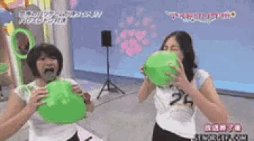 two women are blowing up green balloons with their mouths .