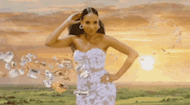 a woman in a white dress is standing in front of a sunset holding a bottle of water .