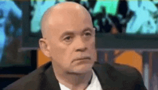 a bald man in a suit and white shirt is making a funny face while sitting on a stage .