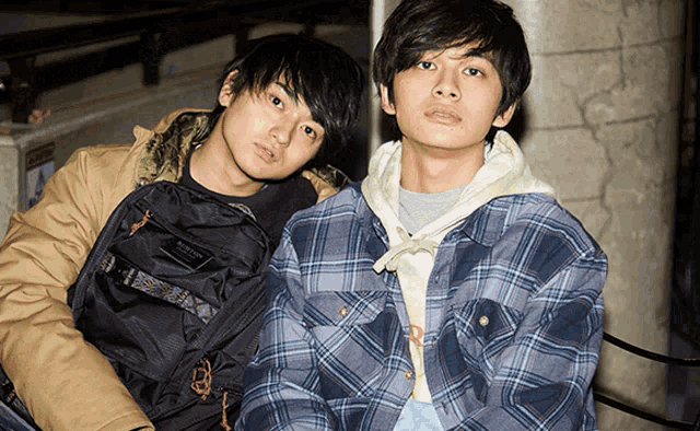 two young men sitting next to each other with one wearing a backpack that says columbia