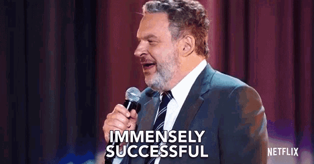 a man in a suit and tie is speaking into a microphone and saying immensely successful .