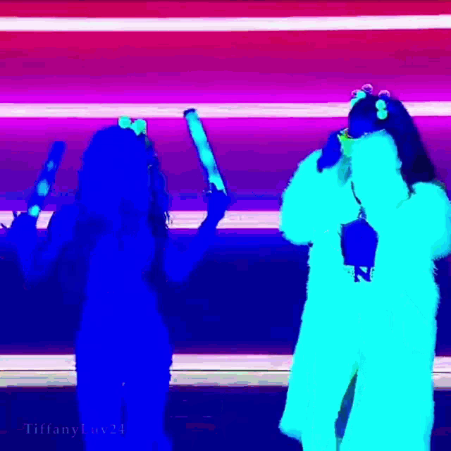 a couple of women standing next to each other in a dark room holding glow in the dark sticks .