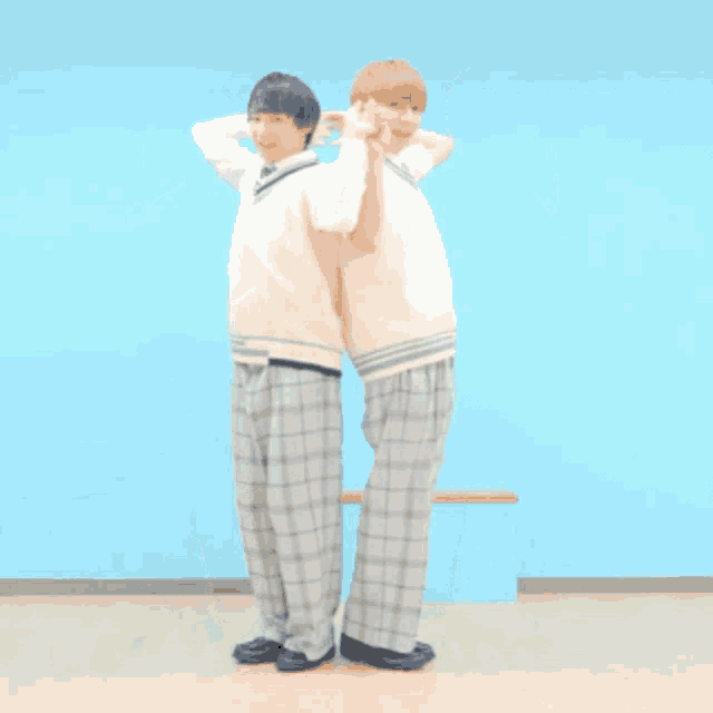 two young men in school uniforms are standing next to each other with their hands in the air