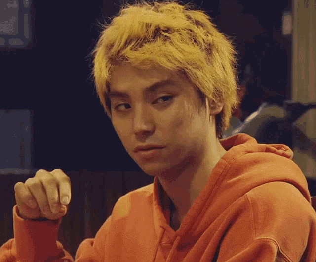 a man with yellow hair is wearing an orange sweater