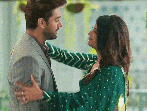 a man in a suit and a woman in a green dress are hugging