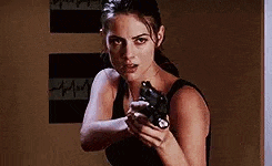 a woman in a black tank top is holding a gun .