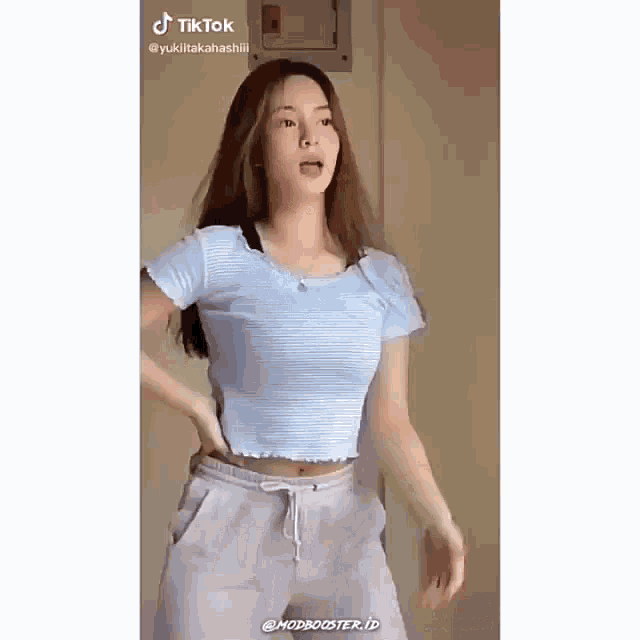 a woman in a blue crop top and gray sweatpants is dancing .