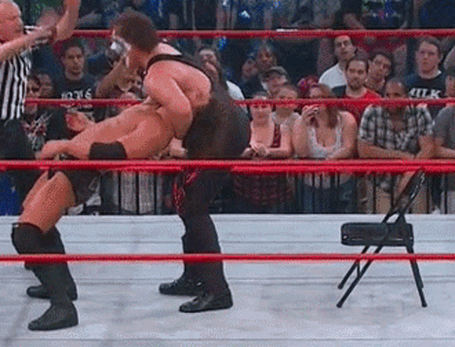 two wrestlers are fighting in a wrestling ring with a referee watching .