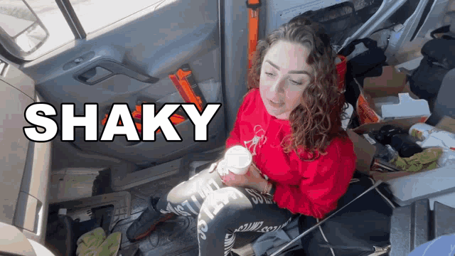 a woman in a red sweatshirt sits in a car with shaky written on the bottom