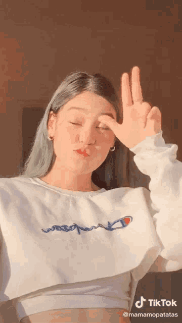 a girl wearing a white champion sweatshirt makes a peace sign