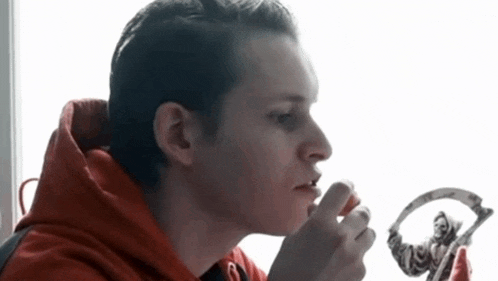 a man in a red hoodie is brushing his teeth with a toothbrush
