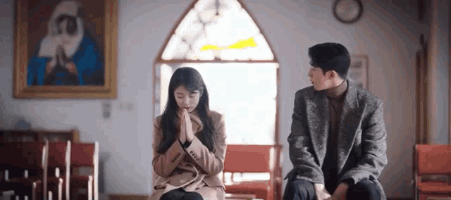 a man and a woman are sitting next to each other in a church with a painting on the wall .