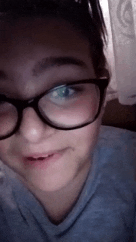 a girl wearing glasses and a blue shirt is making a funny face