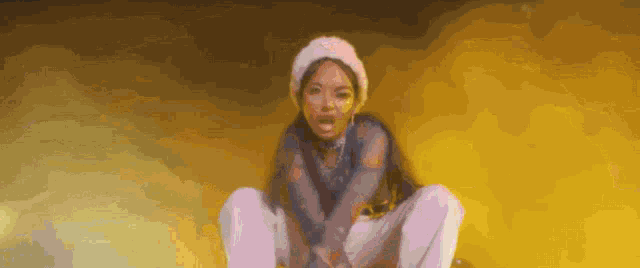 a woman wearing a white hat is squatting down in front of a yellow background