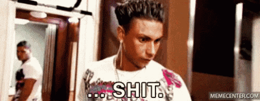 a man wearing a white shirt with the word shit on it is standing in a hallway .