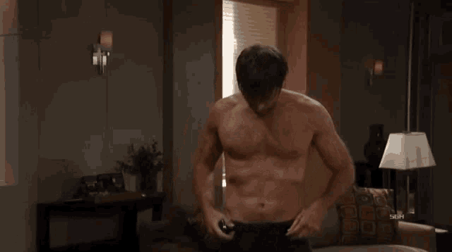 a shirtless man is standing in a living room with his hands on his hips and a sign that says 5kph