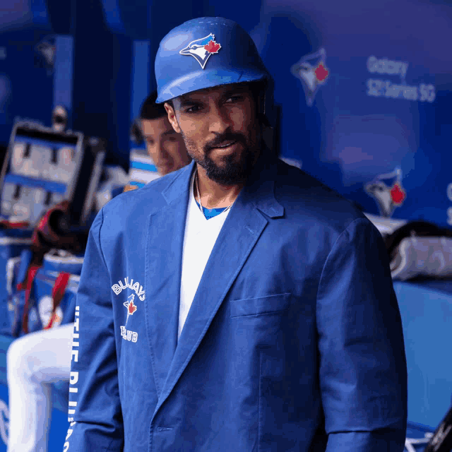 a man wearing a blue jays jacket and helmet stands in a dugout