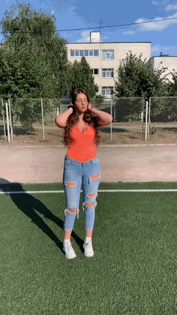 a woman in a red top and ripped jeans is standing on a field