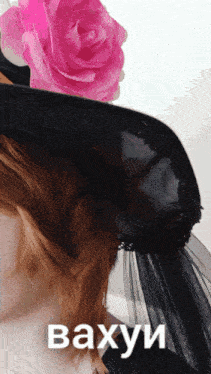 a woman wearing a black hat has a pink rose on her head and the word vaxyu is on the bottom