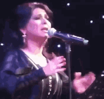 a woman is singing into a microphone on stage in a dark room .