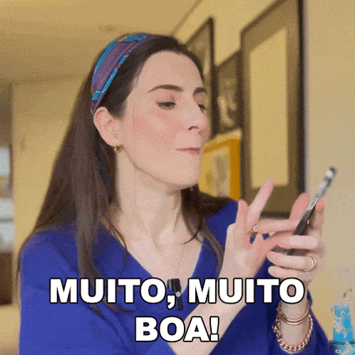 a woman in a blue shirt holds a cell phone and says " muito muito boa "