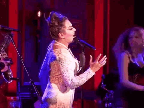 a woman singing into a microphone while a man plays a saxophone in the background